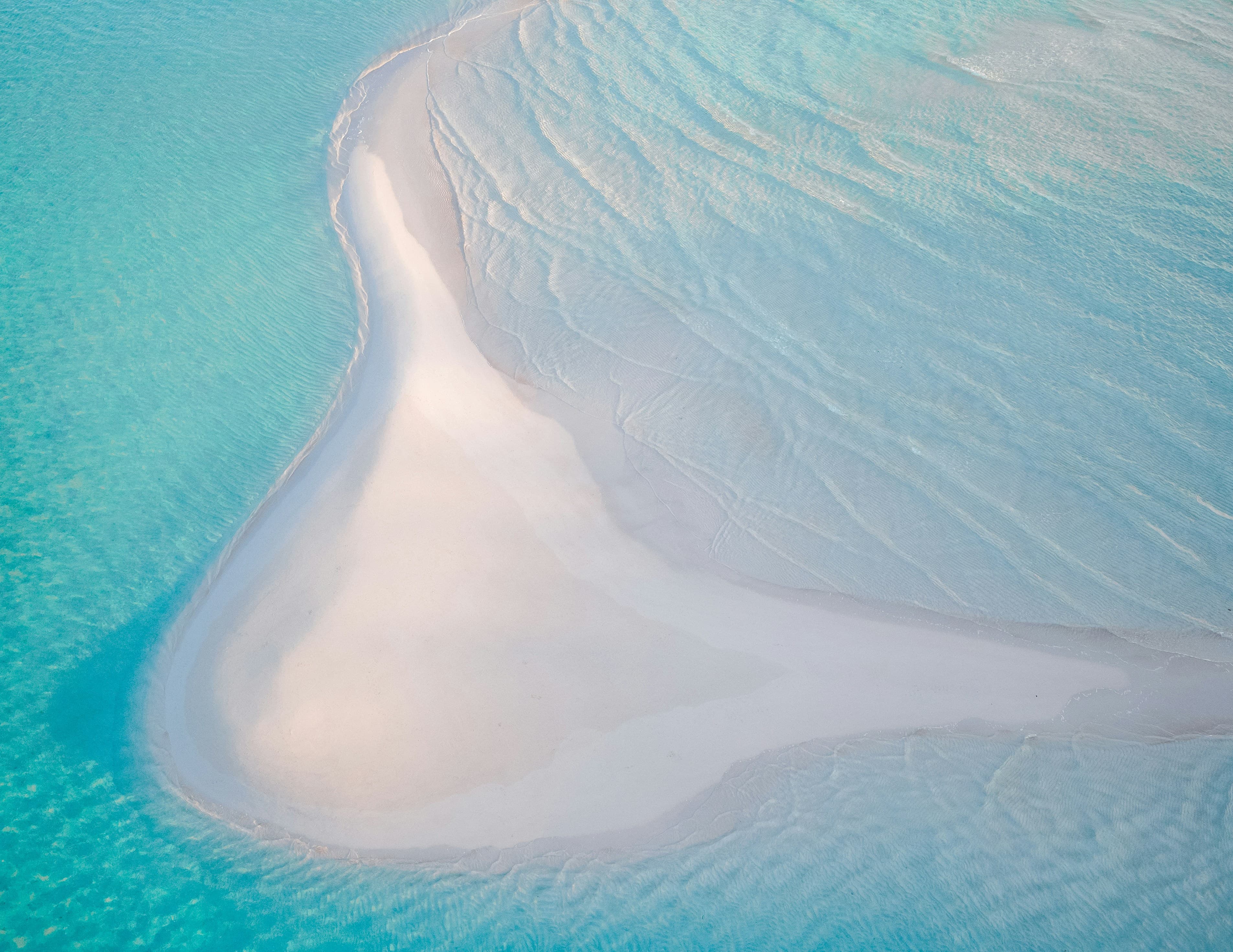 Aerial view of a circular deep blue hole ringed by turquoise shallows